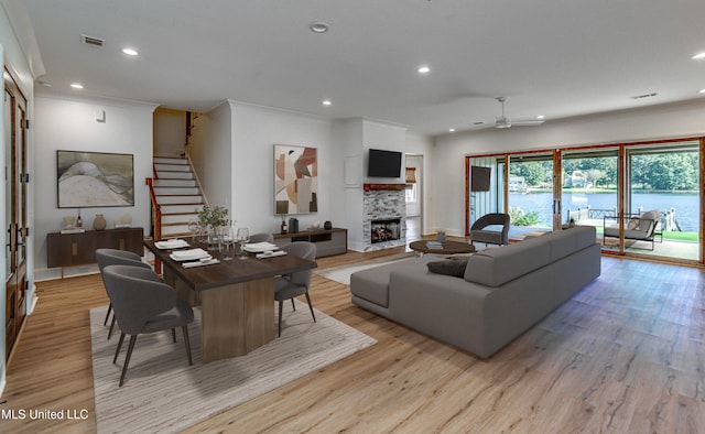 living room featuring ornamental molding, a stone fireplace, light wood-type flooring, and ceiling fan