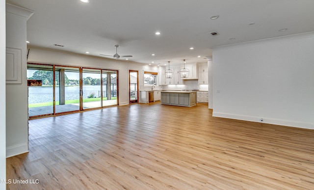 unfurnished living room featuring light hardwood / wood-style flooring, sink, crown molding, and ceiling fan