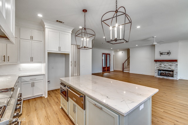 kitchen with a kitchen island, light stone countertops, decorative light fixtures, light wood-type flooring, and white cabinets