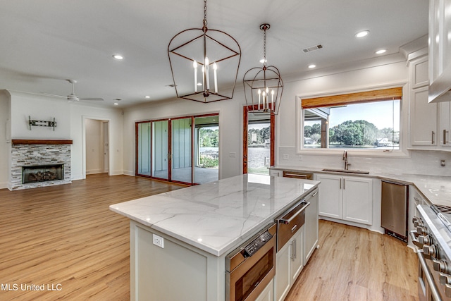 kitchen featuring a center island, white cabinetry, decorative light fixtures, high end stove, and light hardwood / wood-style flooring