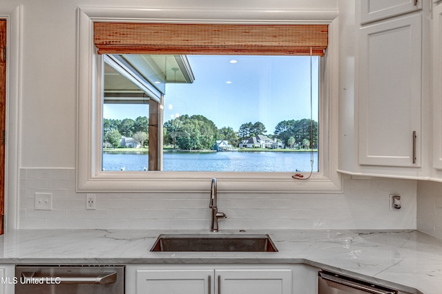 interior space featuring stainless steel dishwasher, white cabinets, sink, and a water view