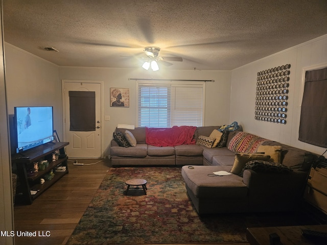living room featuring a ceiling fan, dark wood-style floors, visible vents, ornamental molding, and a textured ceiling