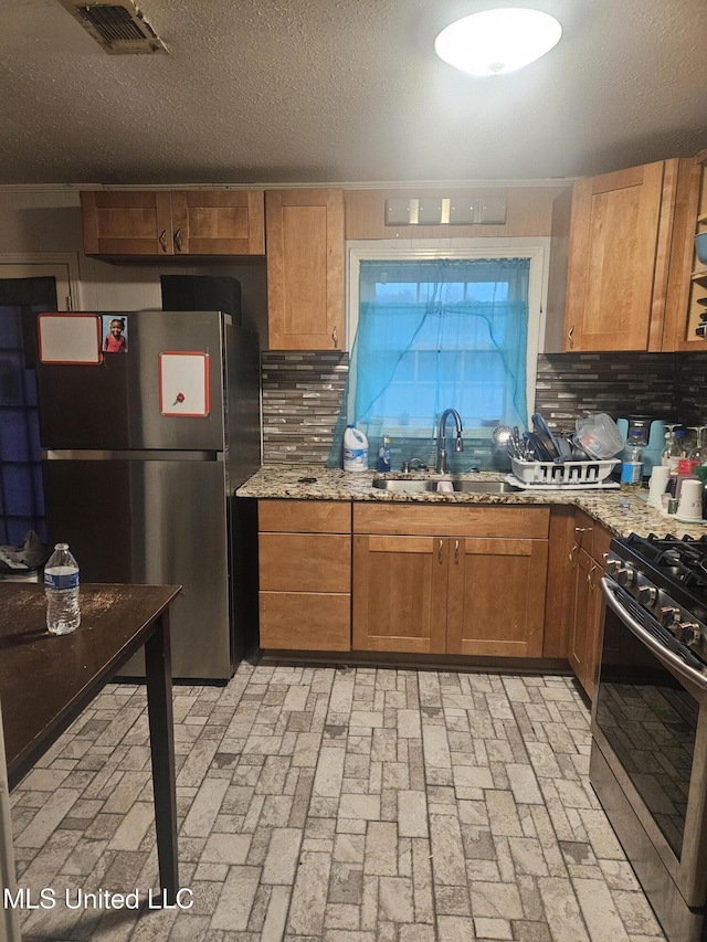 kitchen with light stone countertops, visible vents, a sink, decorative backsplash, and stainless steel appliances