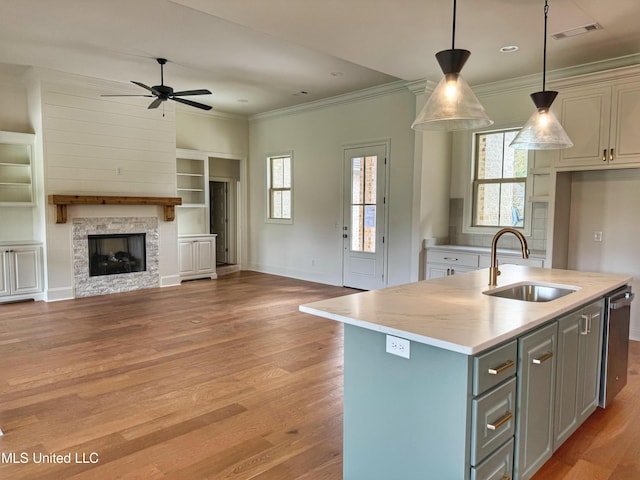 kitchen with built in shelves, sink, a stone fireplace, an island with sink, and pendant lighting