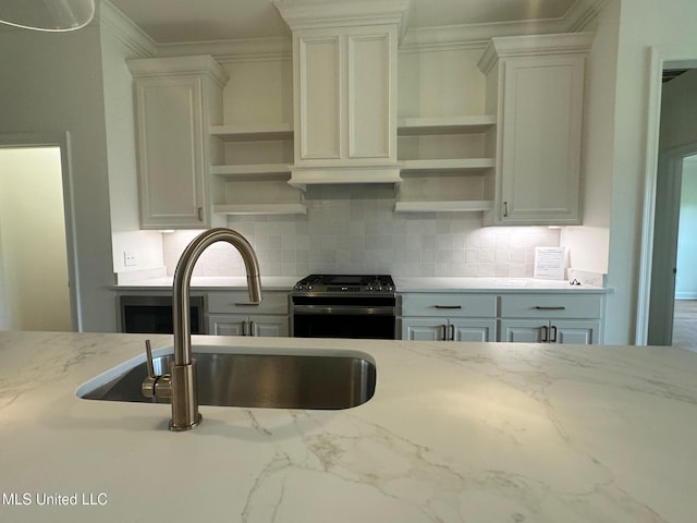 kitchen featuring decorative backsplash, light stone counters, sink, and stainless steel stove