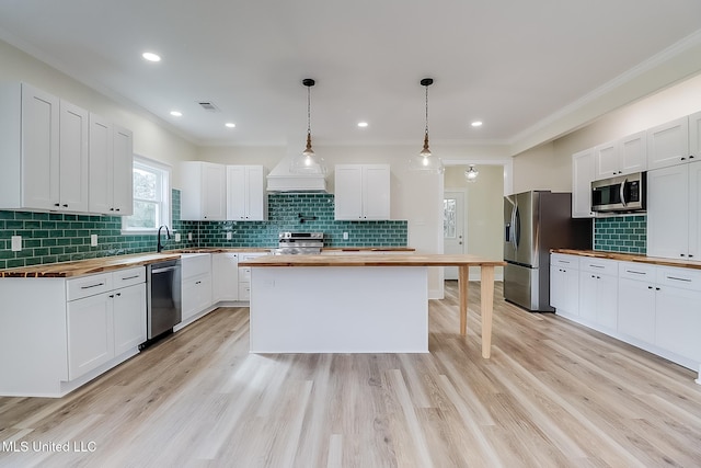 kitchen with pendant lighting, appliances with stainless steel finishes, butcher block countertops, and white cabinets