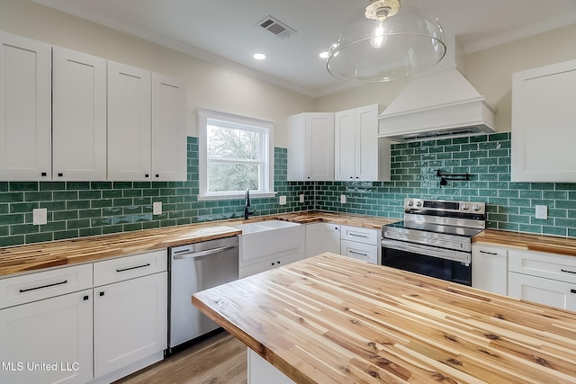 kitchen with stainless steel appliances, wood counters, and white cabinetry