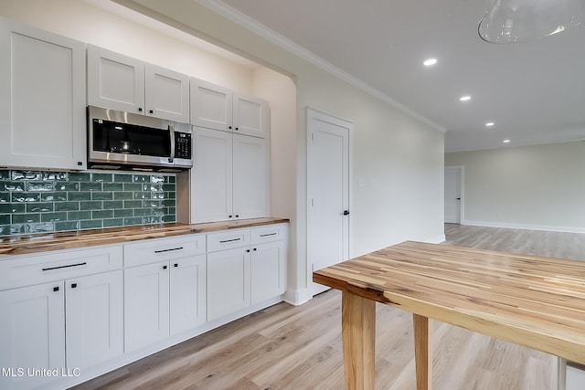 kitchen featuring crown molding, stainless steel microwave, decorative backsplash, and white cabinets