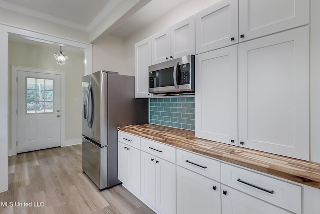 kitchen with white cabinets, butcher block countertops, ornamental molding, hanging light fixtures, and stainless steel appliances