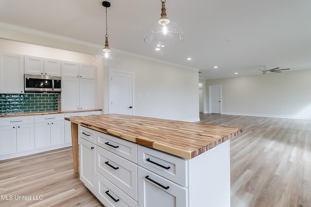 kitchen featuring decorative light fixtures, stainless steel microwave, white cabinets, a kitchen island, and wood counters