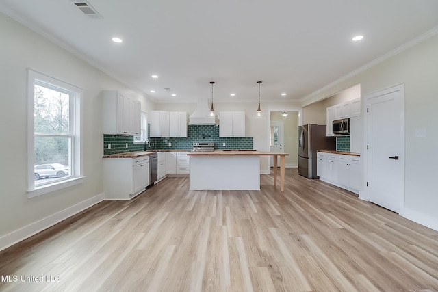 kitchen with a center island, decorative light fixtures, visible vents, appliances with stainless steel finishes, and white cabinets