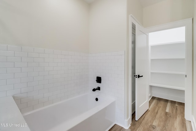 full bath featuring a spacious closet, a tub to relax in, and wood finished floors