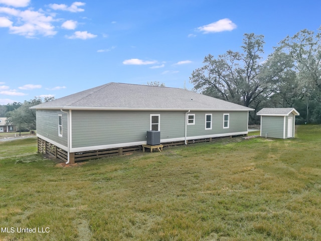 rear view of house featuring a shed, roof with shingles, a lawn, and an outdoor structure