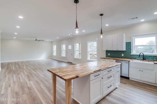 kitchen featuring butcher block countertops, open floor plan, hanging light fixtures, white cabinetry, and stainless steel dishwasher