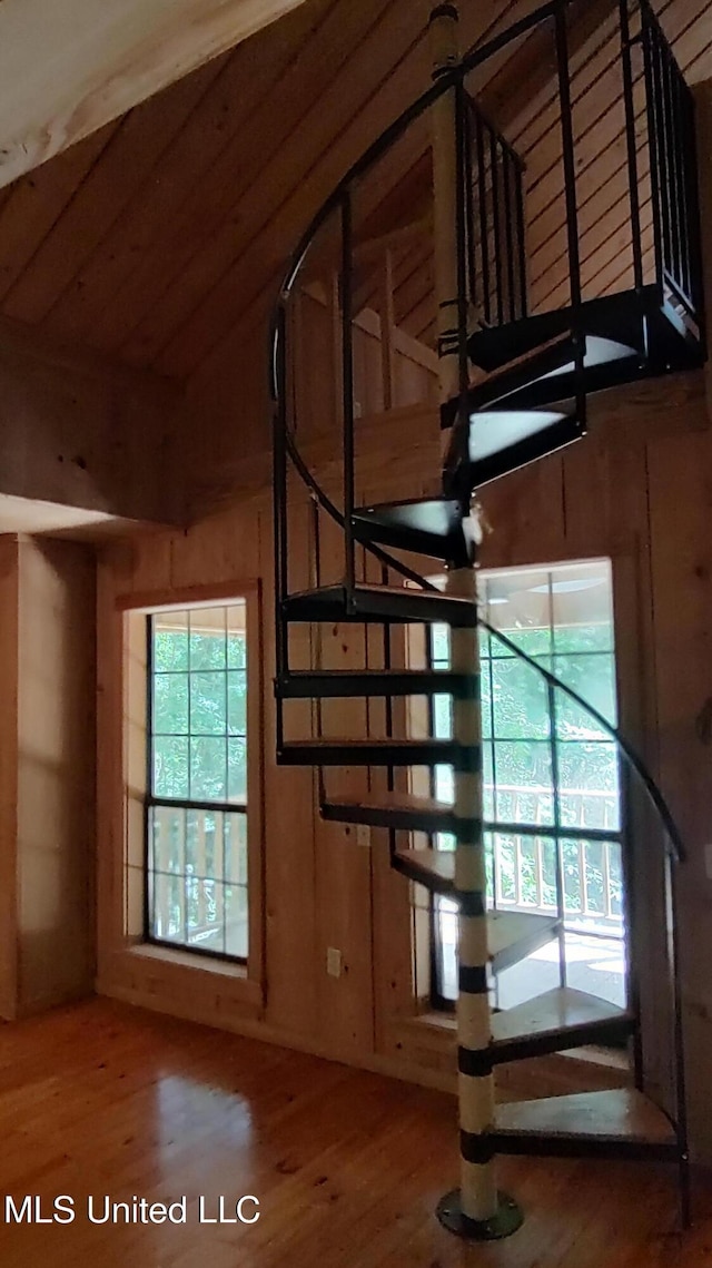 staircase with wood walls, vaulted ceiling, and wood finished floors