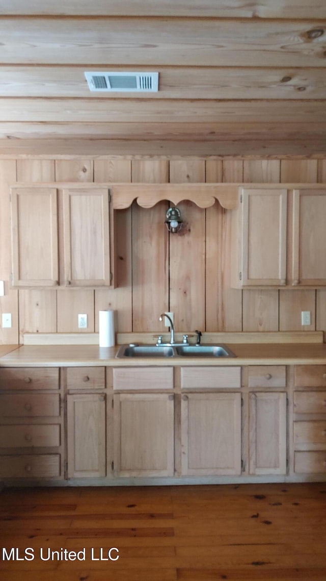 kitchen with wood finished floors, a sink, light brown cabinetry, light countertops, and visible vents