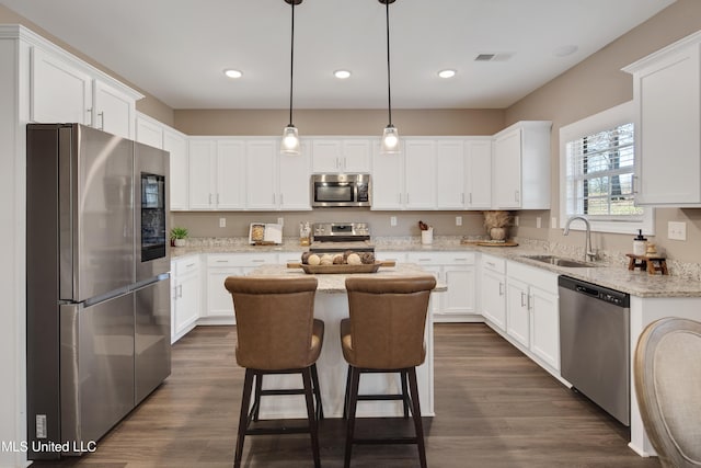 kitchen featuring visible vents, appliances with stainless steel finishes, white cabinets, a sink, and a kitchen island