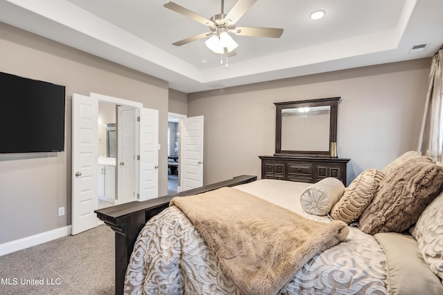 bedroom with carpet floors, a tray ceiling, visible vents, ensuite bathroom, and baseboards