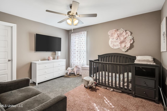 bedroom with a nursery area, carpet flooring, and a ceiling fan