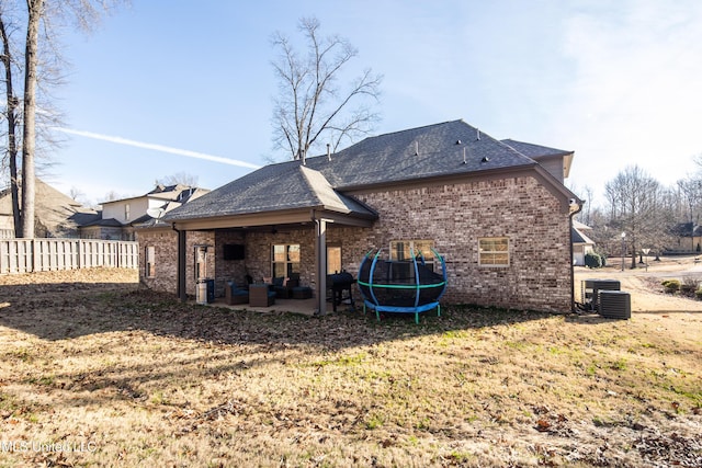 back of property featuring brick siding, a trampoline, fence, and a patio