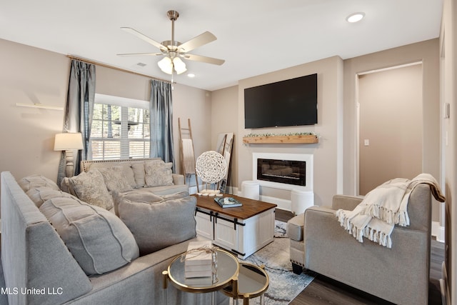 living area featuring recessed lighting, a ceiling fan, a glass covered fireplace, wood finished floors, and baseboards