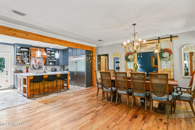 dining room with ornamental molding, sink, a barn door, a notable chandelier, and light hardwood / wood-style floors