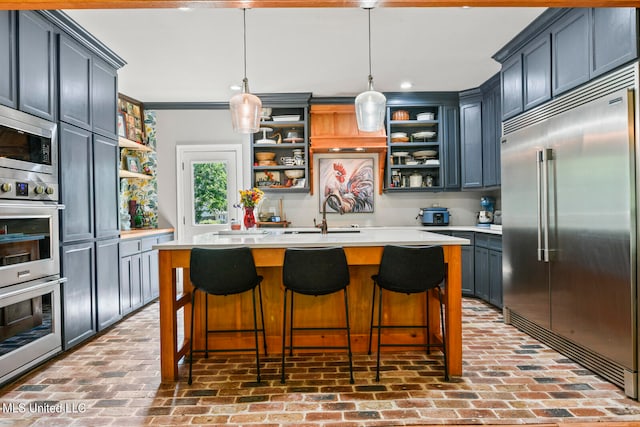 kitchen with ornamental molding, a center island with sink, built in appliances, and pendant lighting