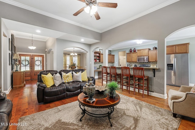 living area featuring crown molding, light wood-style flooring, baseboards, and arched walkways