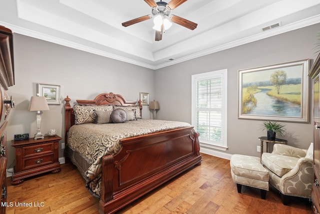 bedroom with visible vents, baseboards, light wood-type flooring, a tray ceiling, and a ceiling fan