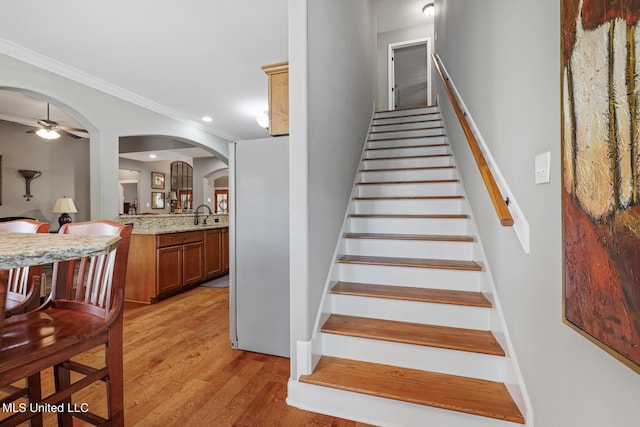 stairway featuring a ceiling fan, wood finished floors, recessed lighting, arched walkways, and ornamental molding