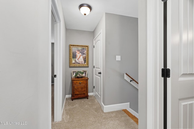 corridor with light colored carpet, an upstairs landing, and baseboards