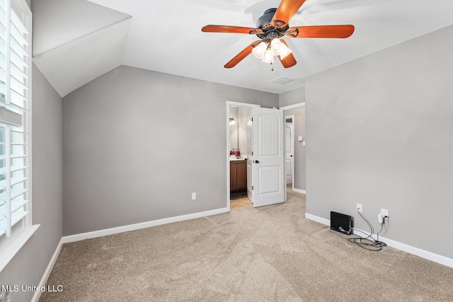 unfurnished bedroom featuring a ceiling fan, baseboards, vaulted ceiling, light carpet, and connected bathroom