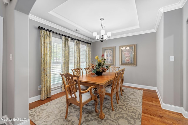 dining space with an inviting chandelier, a raised ceiling, baseboards, and light wood finished floors