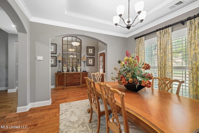 dining room with wood finished floors, arched walkways, visible vents, and a raised ceiling