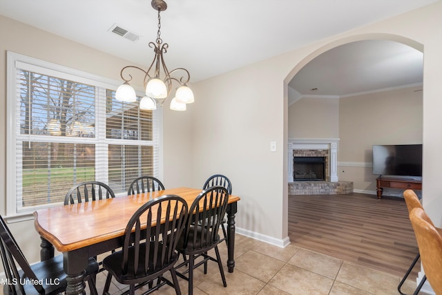 tiled dining space featuring crown molding, a brick fireplace, and a notable chandelier