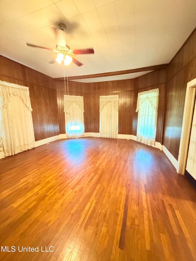 unfurnished room featuring hardwood / wood-style floors, ceiling fan, plenty of natural light, and wood walls