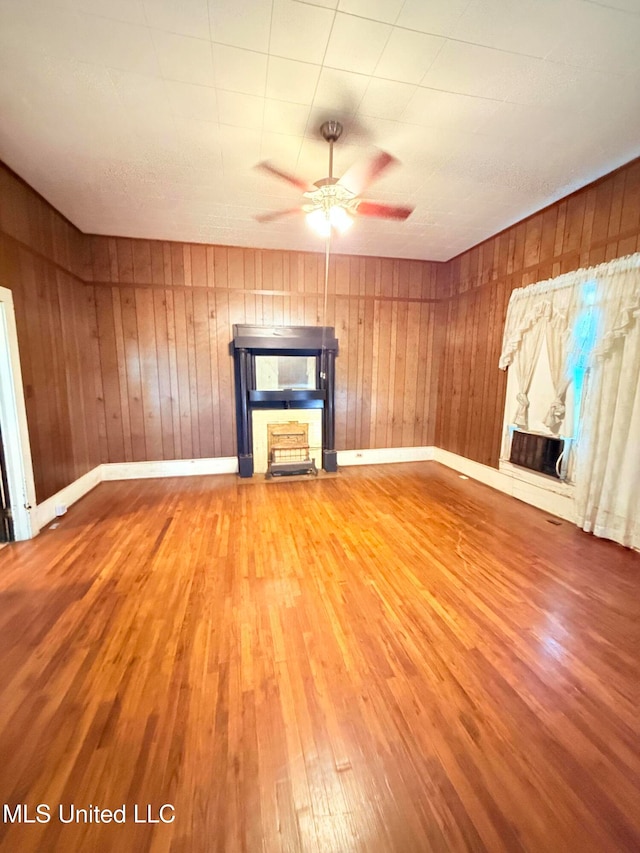 unfurnished living room featuring wooden walls, hardwood / wood-style flooring, and ceiling fan