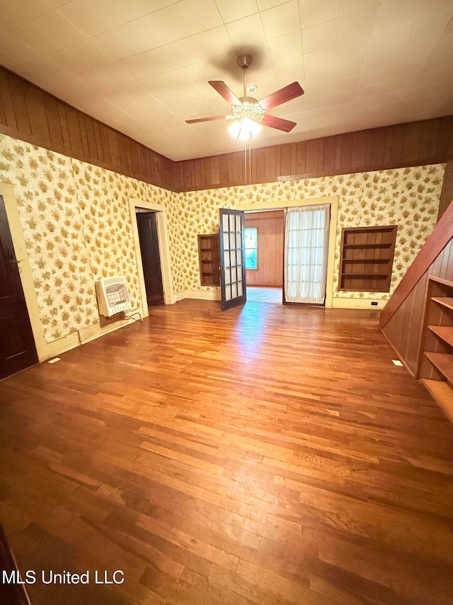 unfurnished living room featuring wood walls, hardwood / wood-style flooring, and ceiling fan