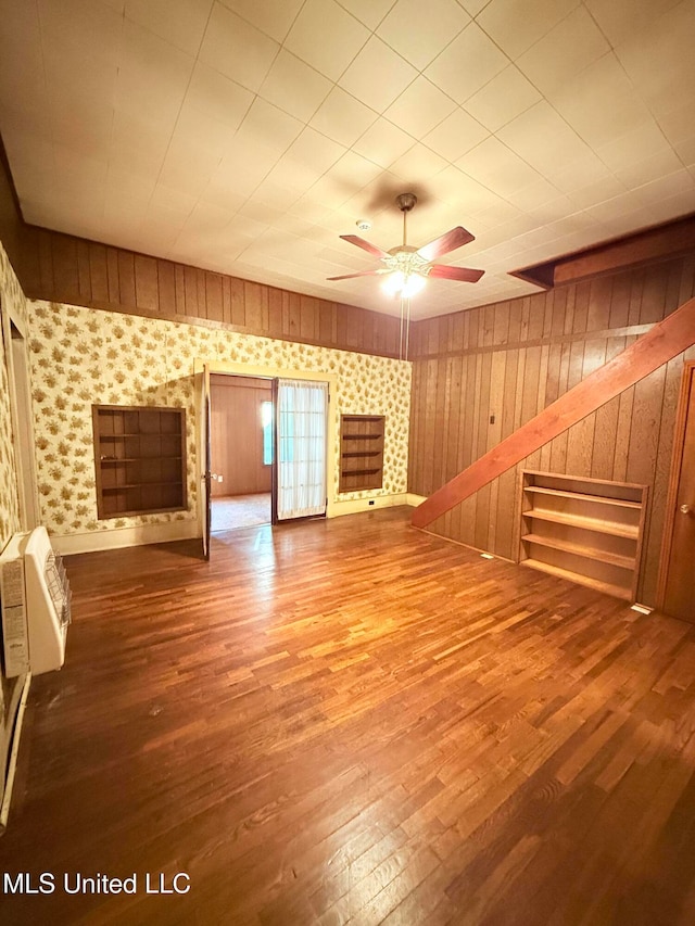 unfurnished living room featuring ceiling fan, wood-type flooring, wooden walls, and a wall mounted AC