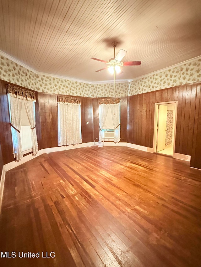 spare room with ornamental molding, wood-type flooring, ceiling fan, and wooden walls