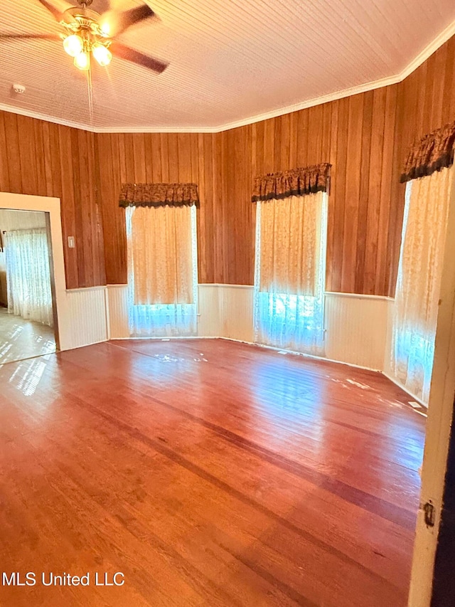 unfurnished room with wood walls, ceiling fan, wood-type flooring, and crown molding