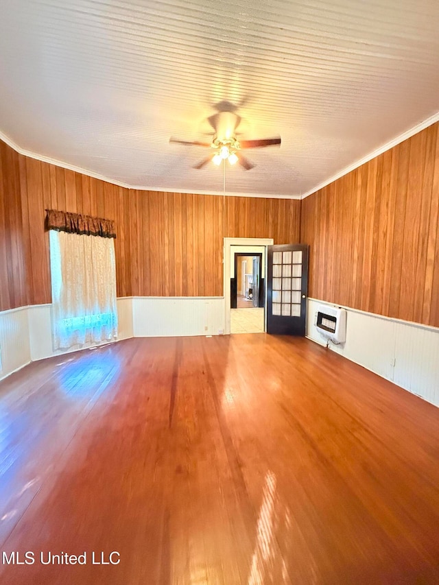 unfurnished living room featuring wood walls, hardwood / wood-style flooring, ornamental molding, ceiling fan, and heating unit