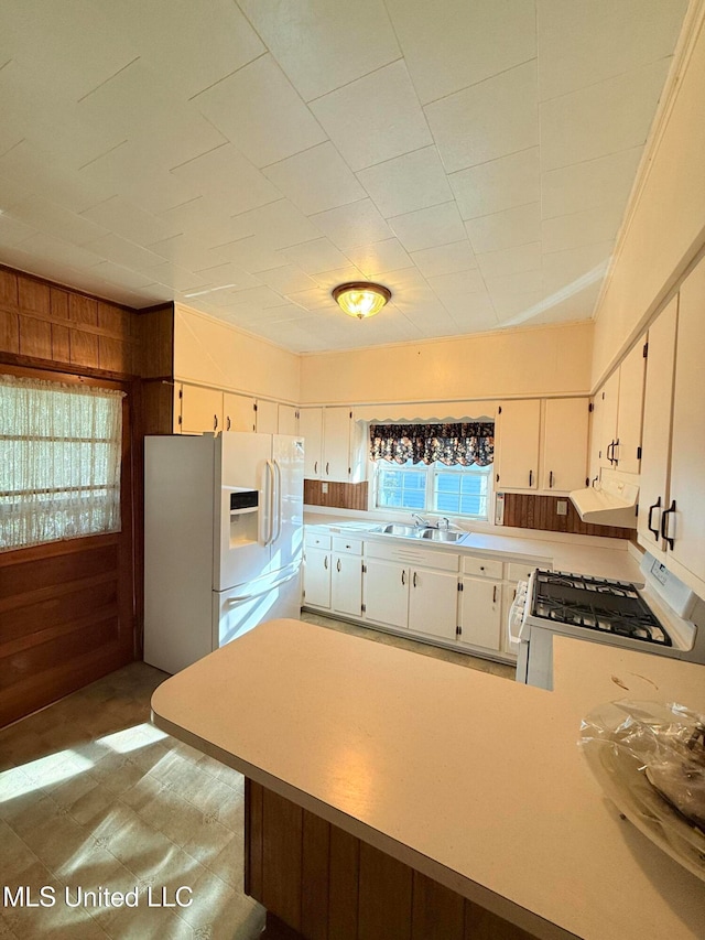 kitchen featuring wood walls, white cabinetry, sink, kitchen peninsula, and white appliances