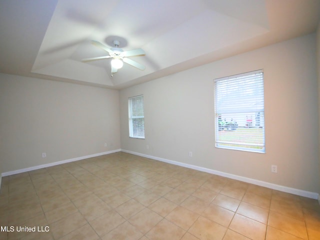 spare room featuring ceiling fan, a tray ceiling, light tile patterned flooring, and baseboards