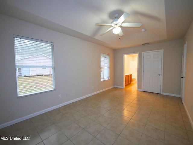 spare room with ceiling fan, light tile patterned floors, visible vents, baseboards, and a tray ceiling