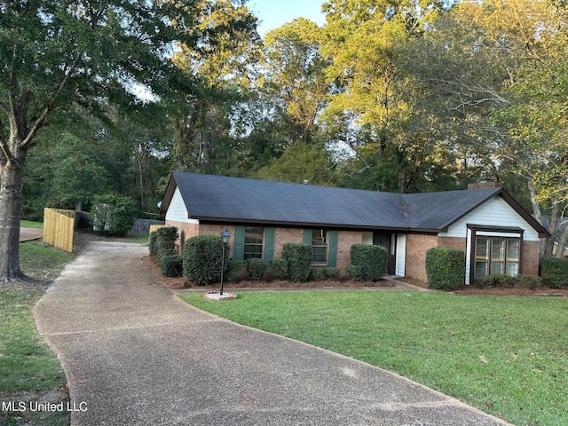 ranch-style home with a chimney, a front lawn, brick siding, and driveway