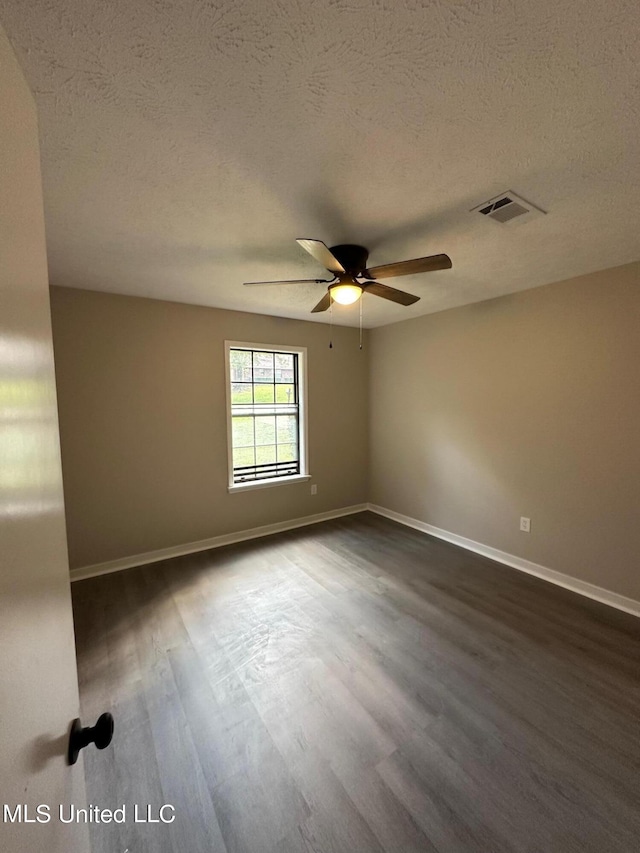 spare room with dark wood finished floors, visible vents, a ceiling fan, baseboards, and a textured ceiling