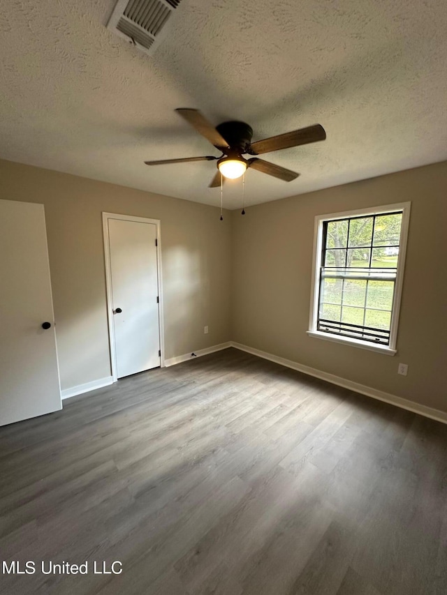 empty room with a textured ceiling, dark wood finished floors, baseboards, visible vents, and ceiling fan
