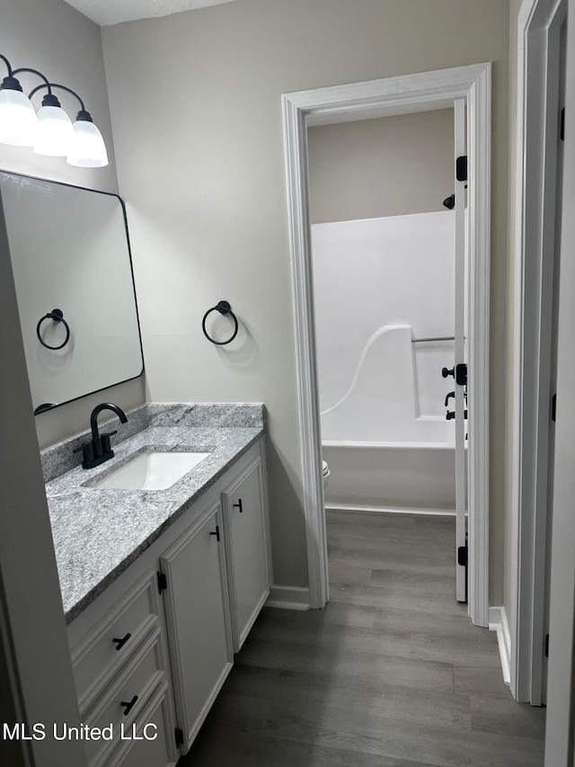 bathroom with baseboards, wood finished floors, vanity, and shower / washtub combination