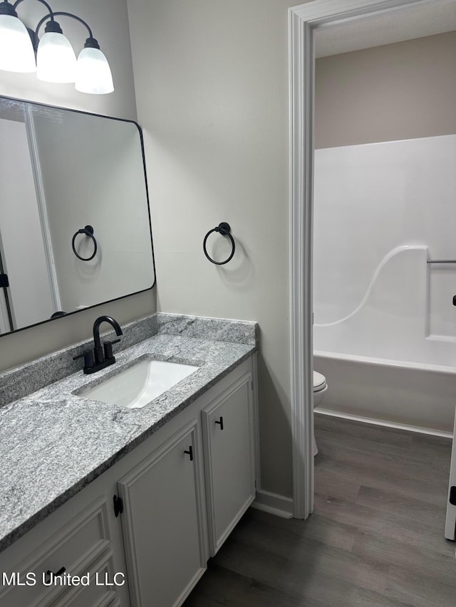 bathroom featuring baseboards, wood finished floors, toilet, and vanity